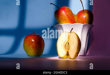 Nahaufnahme von Äpfeln in einem Behälter auf einem rosa und blauen Hintergrund Stockfoto