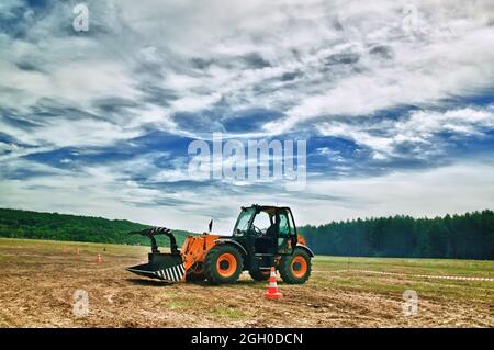 Traktorlader mit einem Eimer auf dem Feld auf Waldgrund. Tonung. Stockfoto