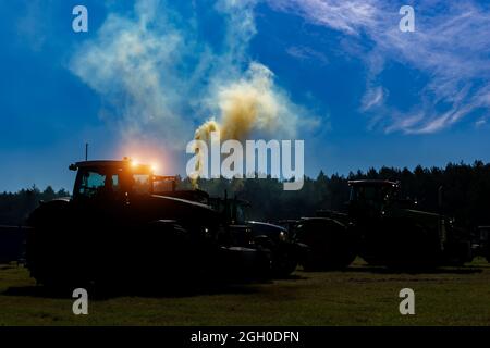 Silhouette eines Traktors auf dem Feld mit den enthaltenen leuchtenden Scheinwerfern in der Nacht auf einem Hintergrund des Himmels . Stockfoto