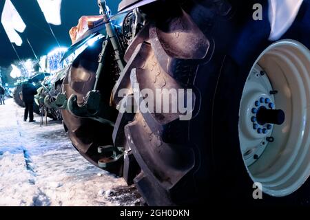 Traktoren stehen in einer Reihe auf einer Winterstraße. Ansicht der Gummireifen. Stockfoto