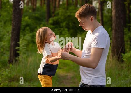 Kaukasisches Mädchen von 6 Jahren, das die Hand des Vaters hält und sich im Wald anschaut. Vater und Tochter spielen zusammen, lachen und haben Spaß. Glücklich Stockfoto