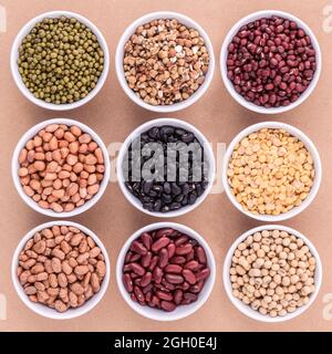 Gemischte Bohnen und Linsen in die weiße Schüssel auf braunem Hintergrund. mung Bean, Erdnuß, Soja, rote Kidney-bohnen, Schwarze Bohne, rote Bohnen, grüne Bohne, mille Stockfoto