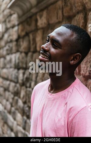 Vertikales Porträt eines afro-amerikanischen jungen Mannes. Er blickt auf eine Seite in der Nähe einer Steinmauer Stockfoto