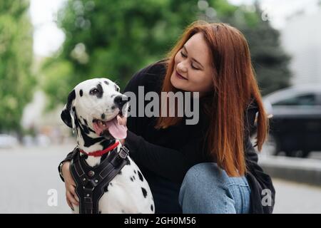 Glückliche Frau posiert und spielt mit ihrem dalmatinischen Hund während eines Stadtspaziergangs. Freundschaft, Liebe und Fürsorge Konzept Stockfoto