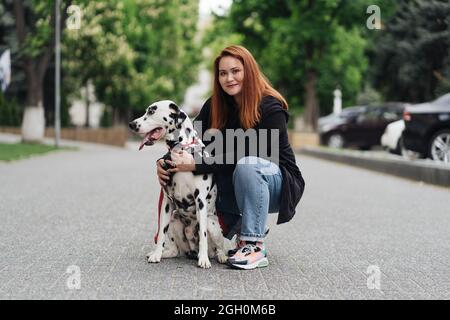 Glückliche Frau posiert und spielt mit ihrem dalmatinischen Hund während eines Stadtspaziergangs. Freundschaft, Liebe und Fürsorge Konzept Stockfoto