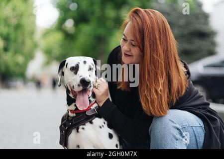 Glückliche Frau posiert und spielt mit ihrem dalmatinischen Hund während eines Stadtspaziergangs. Freundschaft, Liebe und Fürsorge Konzept Stockfoto