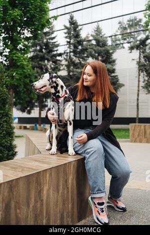 Glückliche Frau posiert und spielt mit ihrem dalmatinischen Hund während eines Stadtspaziergangs. Freundschaft, Liebe und Fürsorge Konzept Stockfoto