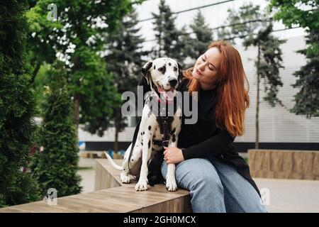 Glückliche Frau posiert und spielt mit ihrem dalmatinischen Hund während eines Stadtspaziergangs. Freundschaft, Liebe und Fürsorge Konzept Stockfoto