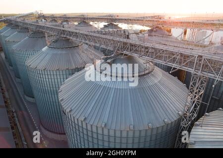 Getreideterminals des modernen Handelshafens. Silos zur Lagerung von Getreide in Strahlen untergehenden Sonnenlichtes, Draufsicht vom Quadcopter. Industrieller Hintergrund. Logist Stockfoto