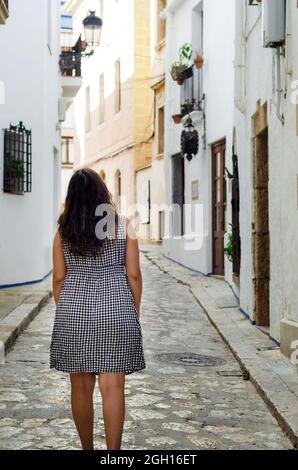 Touristenfrau, die in der Gasse von Sitges, Spanien, spazieren geht. Junge Frau, die in ihrem Urlaub eine enge Straße entlang schlendert. Stockfoto