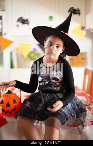 Porträt eines kleinen kaukasischen Mädchens im Hexenkostüm mit einem Kürbis in der Hand. Halloween-Feier. Stockfoto