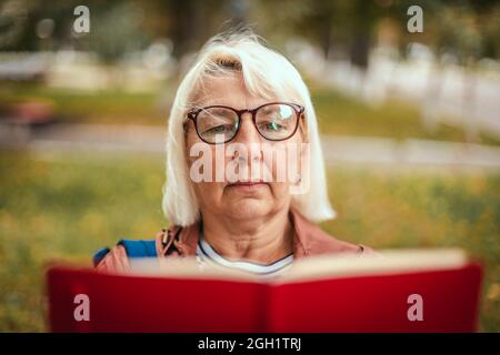 Nahaufnahme einer Frau, die ein Buch liest, während sie sich im Park entspannt Stockfoto