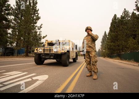 SPC der US-Armee. Dace Taylor von der 270. Militärpolizei der kalifornischen Armee, passt den Kinnriemen seines Helms an, während er am 1. September 2021 mit einem anderen Soldaten in South Lake Tahoe, Kalifornien, spricht, als das Caldor-Feuer in die evakuierte Stadt eingreift. CAL Guard aktivierte am 30. August 150 Militärpolizei, um die kalifornische Autobahnpatrouille mit Kontrollpunkten bei harten Schließungen zu unterstützen, während das Gebiet evakuiert wird. (USA Foto der Air National Guard von Staff Sgt. Crystal Housman) Stockfoto