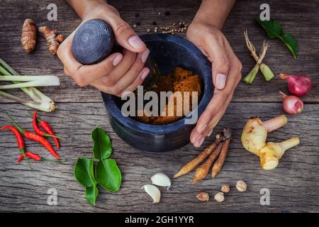 Die Frauen halten mit Mörser und Pistill Spice einfügen. Roten paste Zutaten für Rot auf rustikalen Holzmöbeln Hintergrund Curry. Gewürze Zutaten Chili, Pfeffer, Stockfoto