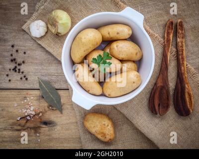 Frische organische Kartoffeln in weißer Keramik Schüssel mit Zutaten und Kräuter, Petersilie, Knoblauch, Lorbeer, Pfeffer, Zwiebel und Himalaya Pink salt auf Hanf s Stockfoto