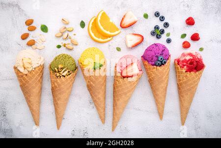 Verschiedene Eis Geschmack in Kegel Heidelbeere, Pistazie, Mandel, Orange und Kirsche Setup auf weißem Stein Hintergrund. Sommer und Süße Menükonzept. Stockfoto