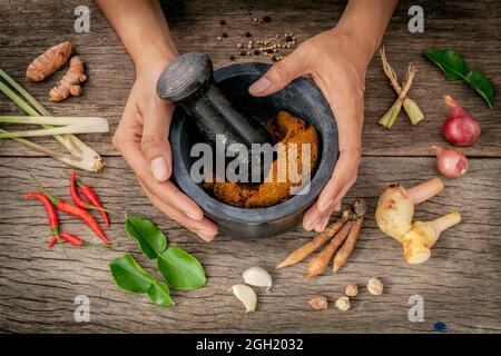 Die Frauen halten mit Mörser und Pistill spice Red Curry Paste Wirkstoff von Thai beliebte Speisen auf rustikalen Holzmöbeln Hintergrund. Gewürze Zutaten Chili, pe Stockfoto