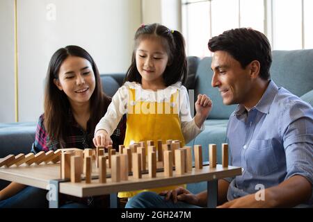 Mischen Sie Rennfamilienliebhaber, kaukasischen Vater und asiatische Mutter mit Halbblut-Tochter spielen Holz Domino Spiel zusammen im Wohnzimmer mit glücklich und Spaß. Id Stockfoto