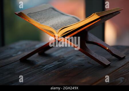 Koran Islamische heilige Buch auf traditionellen muslimischen Stil Holzständer mit orangefarbenem Sonnenlicht und grünen Baum verwischen Hintergrund mit Kopieplatz. Stockfoto