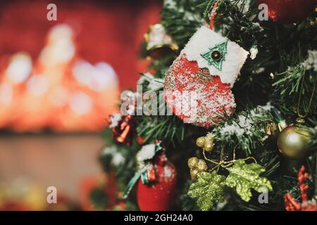 Nahaufnahme von dekorierten Socke hängen auf Kiefer Zweig des Weihnachtsbaums mit einem Ball und verschiedenen Dekor Weihnachten Ornamente decken mit Schneeflocken und Unschärfe BA Stockfoto