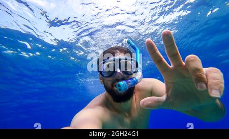 Ein Mann, der mit Schnorcheln beschäftigt ist, schwimmt im Unterwasserreich des Roten Meeres und versucht, an die Oberfläche zu kommen Stockfoto
