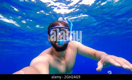 Ein Mann, der mit Schnorcheln beschäftigt ist, schwimmt im Unterwasserreich des Roten Meeres und versucht, an die Oberfläche zu kommen Stockfoto