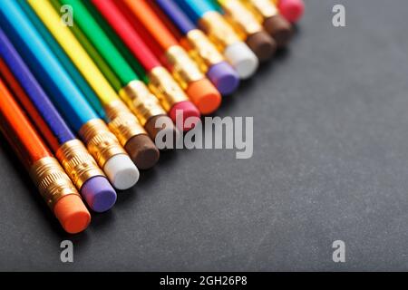 Bunte Bleistifte mit Radiergummis in einer Reihe auf schwarzem Hintergrund. Draufsicht, freier Platz Stockfoto