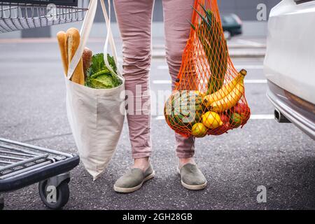 Wiederverwendbare Textil-Einkaufstasche und Netztasche mit gekauften Lebensmitteln. Frau, die auf dem Parkplatz steht, nachdem sie im Supermarkt einkaufen war. Ethischer Konsumdenken Stockfoto