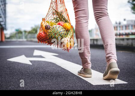 Wählen Sie die richtige Richtung für einen gesunden und nachhaltigen Lebensstil ohne Verschwendung. Frau mit wiederverwendbarem Netzbeutel voller Obst unterwegs Stockfoto