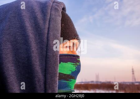 Nahaufnahme eines kaukasischen Mannes mit einem Schal als Maske und einer Winterjacke mit Kapuze. Stockfoto
