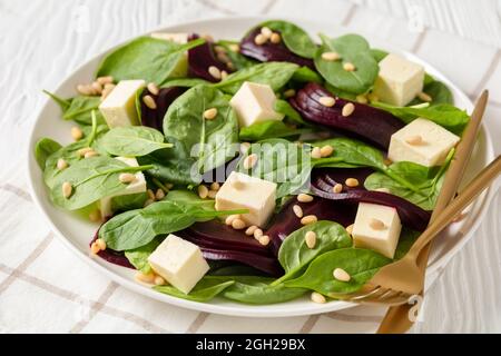 Nahaufnahme von geröstetem Rübensalat mit gewürfeltem Feta-Käse, Pinienkernen und Spinat auf einem weißen Teller mit goldenem Besteck auf einem Holztisch, kanadische Küche Stockfoto