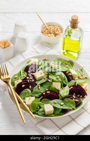 Gerösteter Rübensalat mit gewürfeltem Feta-Käse, Pinienkernen und Spinat auf einem weißen Teller mit goldenem Besteck auf einem Holztisch, kanadische Küche, vertikale VI Stockfoto