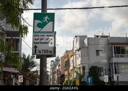 Tel Aviv, Israel - 16. August 2021: Ein mehrsprachiges Schild, das auf eine Tsunami-Evakuierungsroute in einer Straße in Tel Aviv, Israel, zeigt. Stockfoto