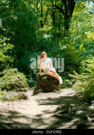 Kind blondes Mädchen sitzt auf einem Felsen am Fluss Sommer Sonnenlicht Stockfoto