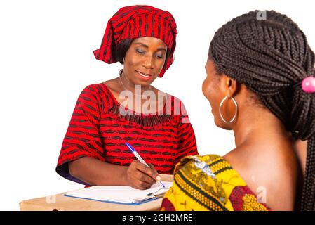 Schöne afrikanische Frau, die in traditioneller Kleidung auf weißem Hintergrund lächelnd ein Dokument signiert, nachdem sie ein Online-Paket erhalten hat. Stockfoto