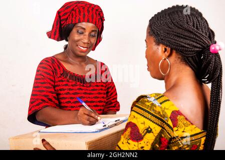 Schöne afrikanische Frau, die in traditioneller Kleidung auf weißem Hintergrund lächelnd ein Dokument signiert, nachdem sie ein Online-Paket erhalten hat. Stockfoto