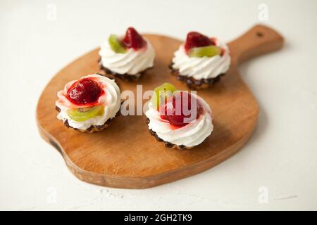 Cupcakes mit Quark auf Vintage-Tablett-leckerer Muffin mit Erdbeere und Kiwi auf Holzplatte Stockfoto