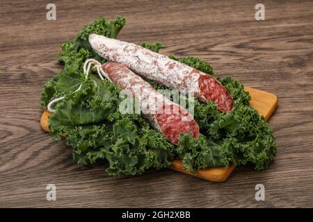 Spanische Fuet-Wurst mit Salatblättern auf Holzhintergrund Stockfoto
