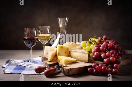 Schneidebrett mit Käsesortiment, Weiß- und Rotweinen mit Trauben auf Holztisch, Platz für Text. Stockfoto