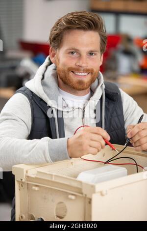 Seitenansicht eines lächelnden, hübschen Elektrikers, der den Schaltkasten repariert Stockfoto