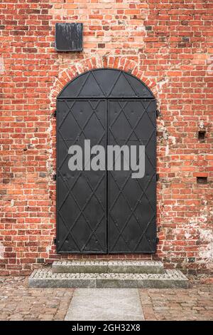 Eiserne Tür in einer roten Backsteinmauer. Gotische Burg der pommerschen Herzöge in Darłowo, Polen. Stockfoto