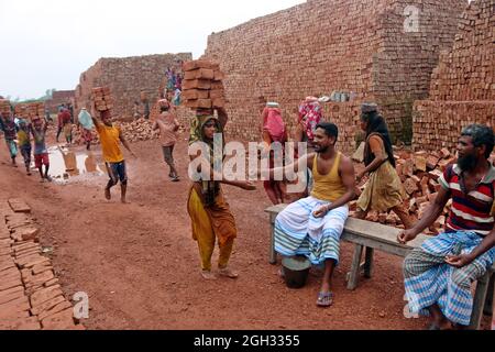 DHAKA, BANGLADESCH - 4. SEPTEMBER: Eine Frau hält Ziegelsteine auf dem Kopf, nachdem sie sie aus den Öfen genommen hat, während sie auf einem Brett den Fluss überquert, um sie auf der anderen Seite bei einem Mauerwerk unterzubringen, um die Ziegelsteine für Bauunternehmen außerhalb von Dhaka zu verteilen. Ziegelfeldarbeiter arbeiten 7 Tage die Woche und werden 350 BDT (4.37 Dollar) pro Tag bezahlt, die Besitzer jeder Ziegelfabrik beschäftigen zwischen 100-200 Arbeiter und arbeiten während der Trockenzeit von Sonnenaufgang bis Sonnenuntergang. Am 4. September 2021 in Dhaka, Bangladesch. (Foto von Habibur Rahman/Eyepix Group/Sipa USA) Stockfoto