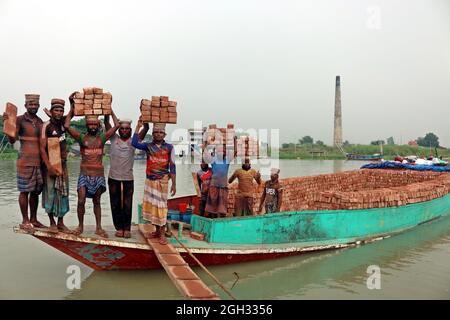 DHAKA, BANGLADESCH, 4. SEPTEMBER: Arbeiter halten Ziegelsteine auf ihren Köpfen, nachdem sie sie aus den Öfen genommen haben, während sie auf einem Brett den Fluss überquert, um sie auf der anderen Seite bei einem Mauerwerk unterzubringen, um die Ziegelsteine für Bauunternehmen außerhalb von Dhaka zu verteilen. Ziegelfeldarbeiter arbeiten 7 Tage die Woche und werden 350 BDT (4.37 Dollar) pro Tag bezahlt, die Besitzer jeder Ziegelfabrik beschäftigen zwischen 100-200 Arbeiter und arbeiten während der Trockenzeit von Sonnenaufgang bis Sonnenuntergang. Am 4. September 2021 in Dhaka, Bangladesch. (Foto von Habibur Rahman/Eyepix Group/Sipa USA) Stockfoto
