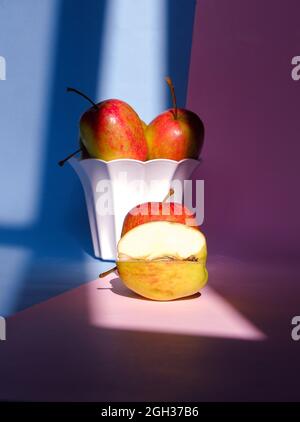 Blick auf den gebissenen Apfel und die WH?le in einer Schüssel auf einem rosa-blauen Hintergrund Stockfoto