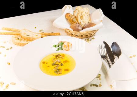 Kürbissuppe mit Kürbiskernen bestreut, Garnelen in einer Zusammensetzung mit Brot, Besteck, Brotstangen auf einem Tisch Stockfoto