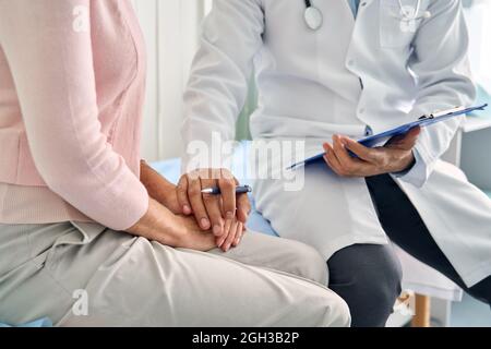 Männlicher Arzt, der ältere ältere weibliche Patientin mit der Hand konsultiert. Stockfoto