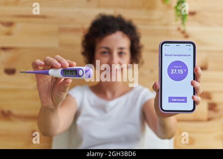 Porträt einer Frau, die die Kamera anschaut, während sie ihre Basaltemperatur misst Stockfoto