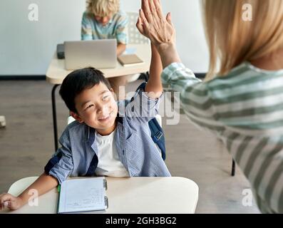 Glücklich asiatische Kind Junge geben hohe fünf zu weiblichen Lehrer in der Klasse im Klassenzimmer. Stockfoto