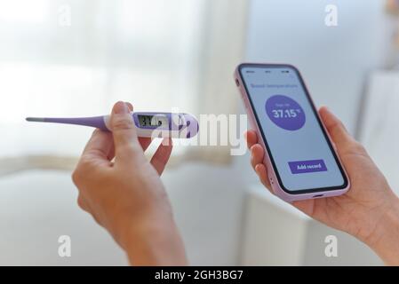 Nahaufnahme der Hände einer Frau, die ihre Basaltemperatur gemessen hat Stockfoto