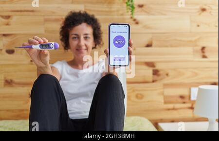 Porträt einer Frau, die die Kamera anschaut, während sie ihre Basaltemperatur misst Stockfoto